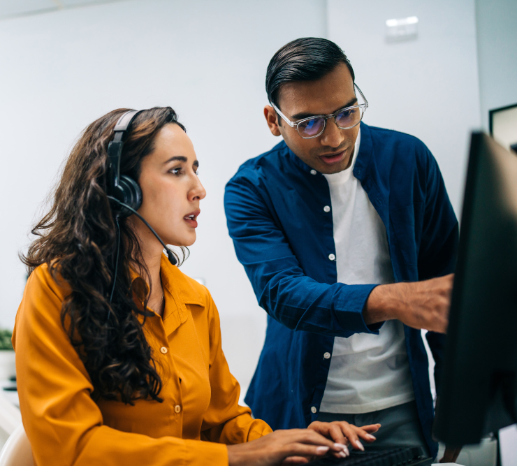Colleague guiding a headset-wearing employee through an AI tool on her screen, representing hands-on enterprise AI training